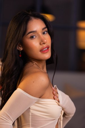 Carolina Guerrero teases in denim shorts and white off shoulder top, legs spread on bed, red earrings gleaming — Carolina Guerrero #5