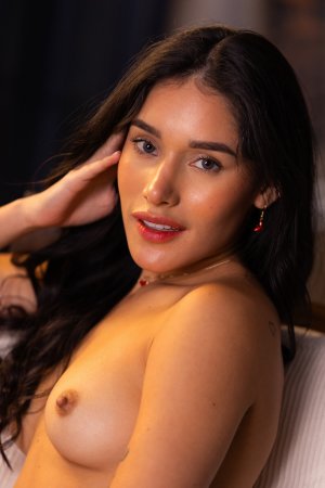 Carolina Guerrero teases in denim shorts and white off shoulder top, legs spread on bed, red earrings gleaming — Carolina Guerrero #24
