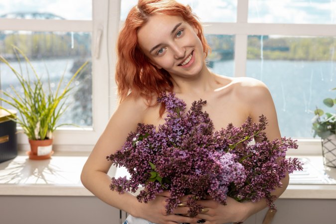 Emma A posing nude with lilac blooms in a sunlit kitchen, her red hair glowing as she teases with parted legs and soft smiles — Emma A #2