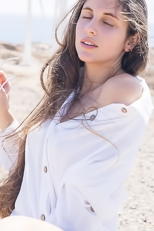 Esfinge bares all on a rocky shore her white shirt slipping as ocean wind teases her curves