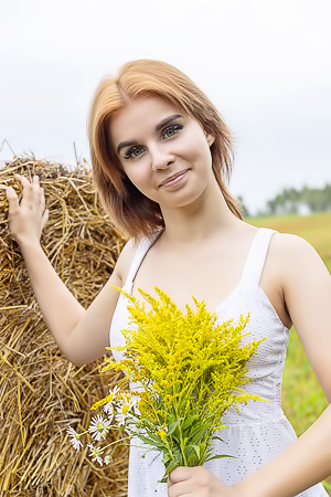 Mari A spreads wide on the haybale, her red hair catching sun as she smiles through the bloom